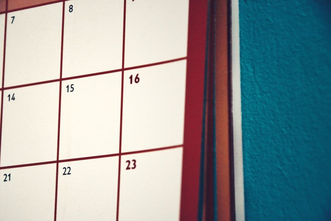 A close view of a paper wall calendar with red grid lines hanging against a teal wall