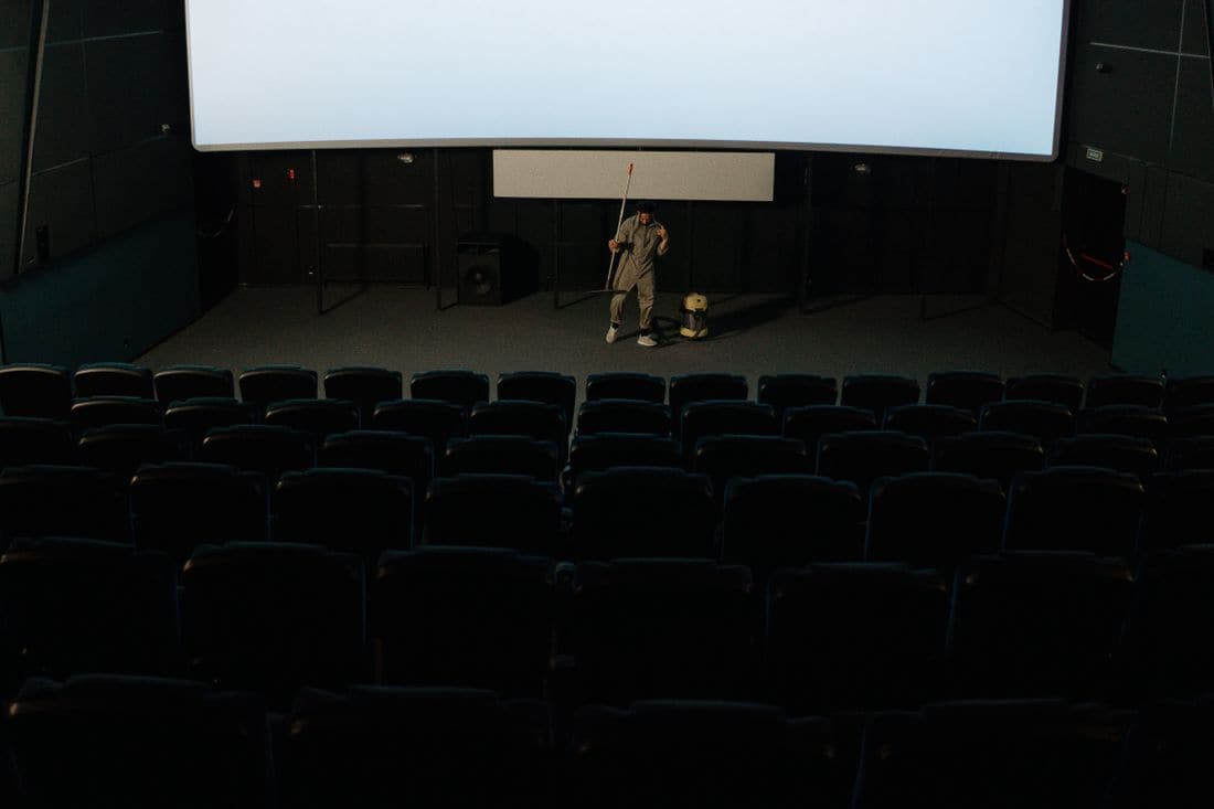 A cleaner vacuuming the floor below the screen in an empty cinema