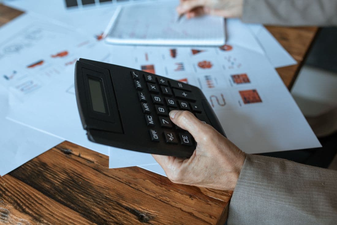A hand holding a calculator over printed charts on a wooden table