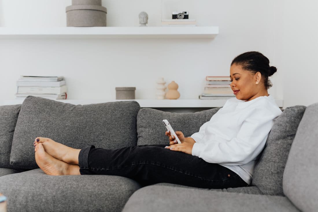 A woman relaxing on a grey sofa at home, checking her phone