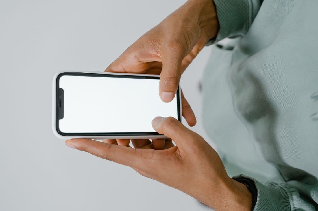 Two hands holding a phone sideways with a blank white screen, in front of a pale green sweatshirt