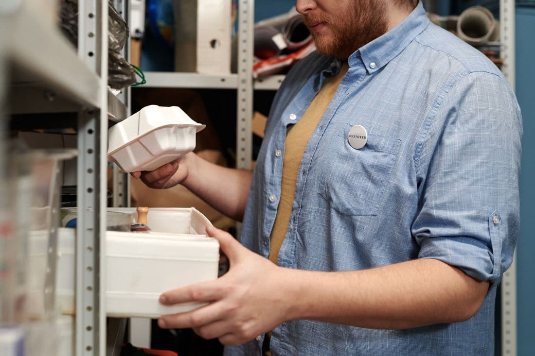 A worker taking plastic containers off storeroom shelves