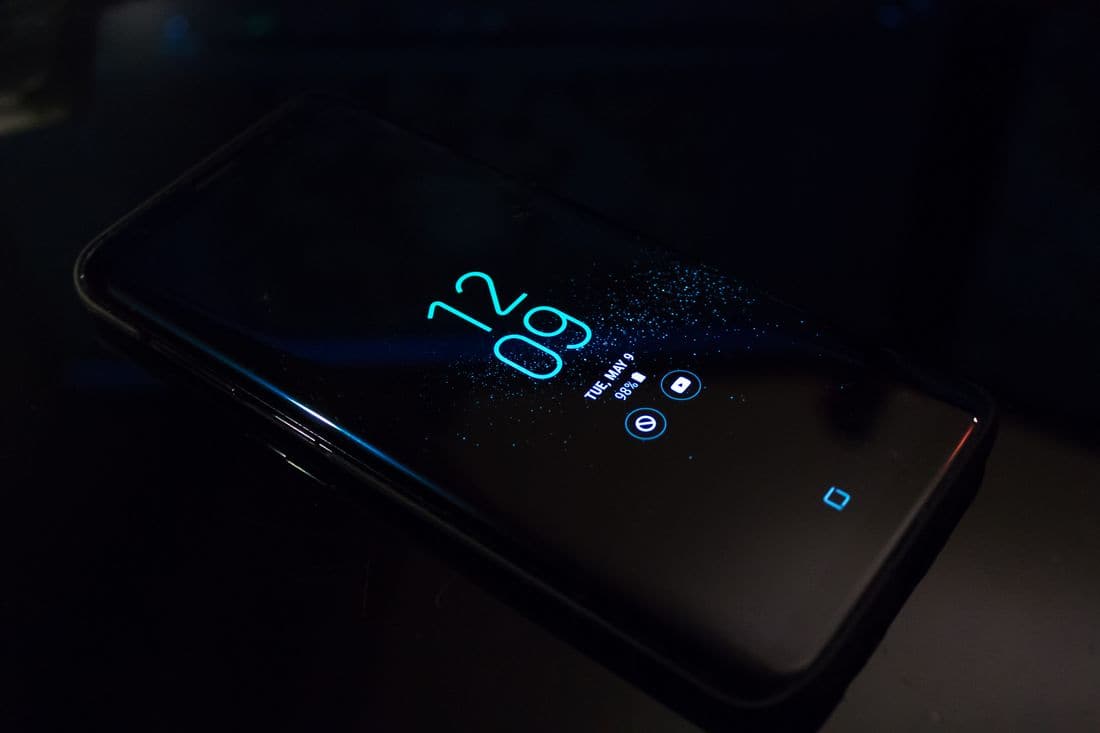 A smartphone lying in the dark with its lock screen lit up in blue, showing the time and date