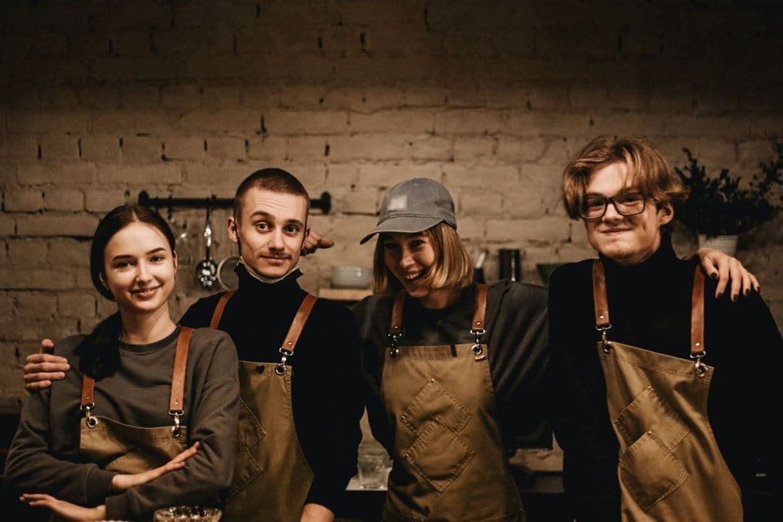 Four cafe workers in aprons standing together behind the counter