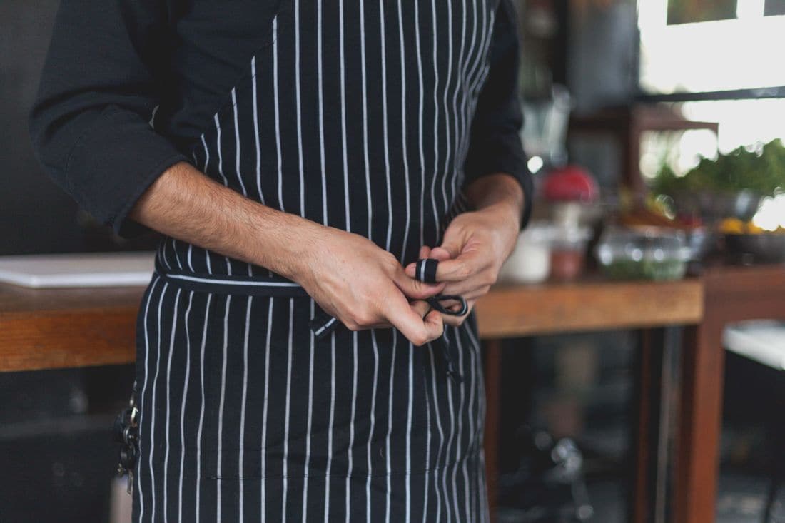 A cook in a black and white striped apron tying its strings in a restaurant kitchen