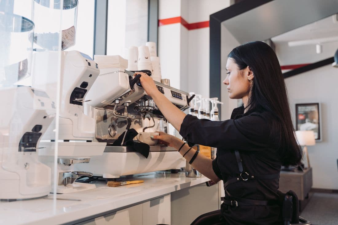 A barista in a black uniform making coffee at a white espresso machine