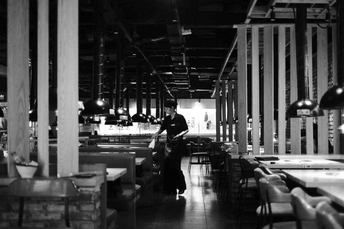 A server clearing a table in an empty restaurant late at night, in black and white