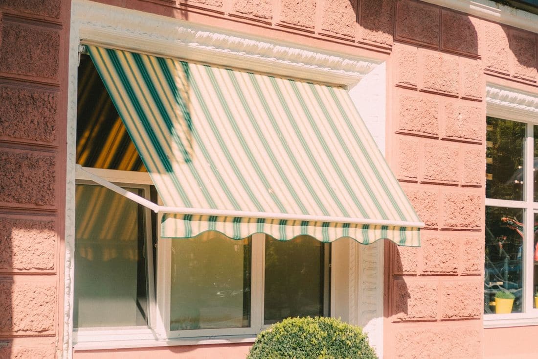 A pink rendered shop building with a striped green and white awning over one front window and a second window beside it