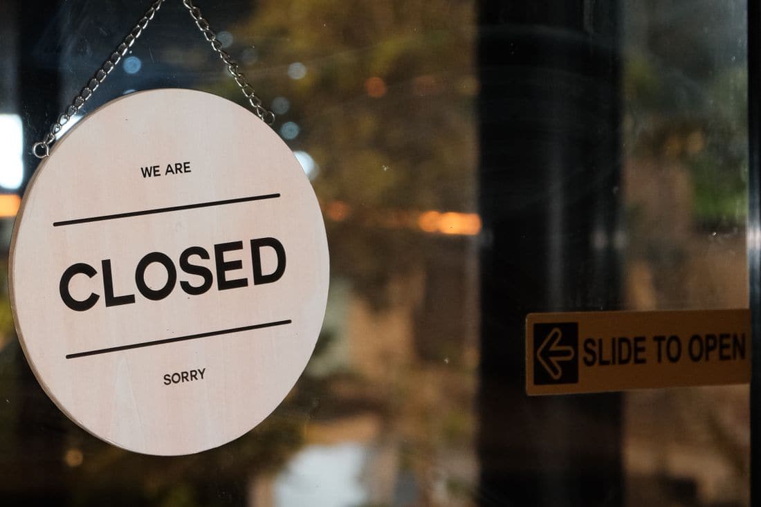 A round wooden sign reading we are closed hanging on a glass door at night beside a slide to open sticker
