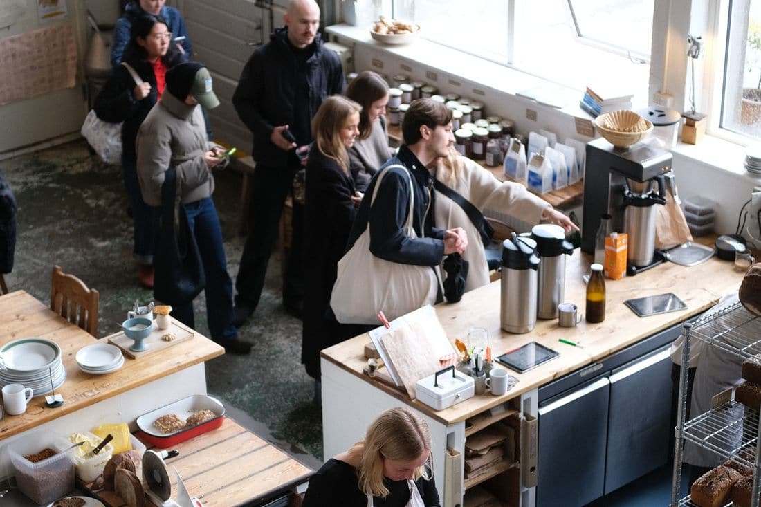 A queue of customers waiting to order at a busy cafe counter, seen from above, with a worker plating food below