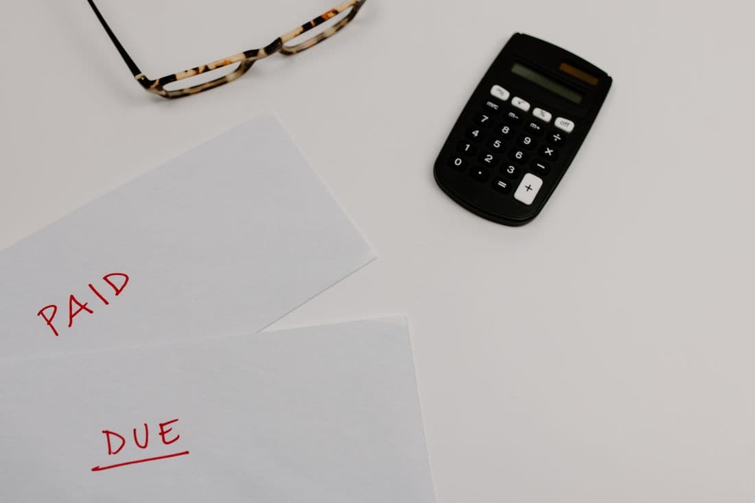 Two papers marked paid and due beside a calculator and a pair of glasses