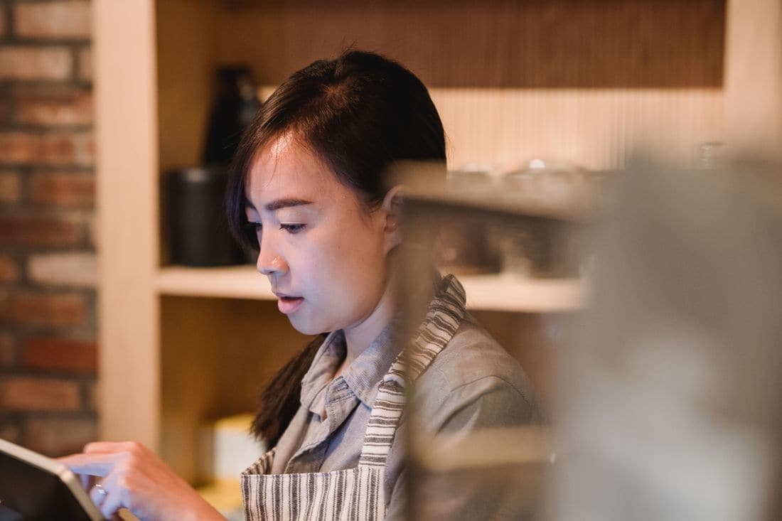A cafe worker in a striped apron tapping on a tablet behind the counter