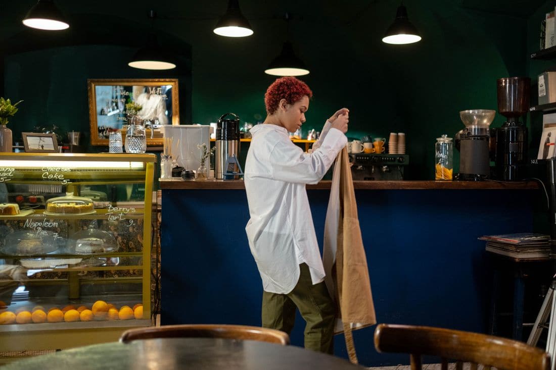 A barista in a white shirt tying on an apron behind the counter of a quiet cafe before opening