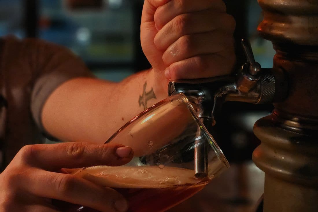 Close-up of a bartender’s hand pulling a beer tap to fill a glass at a dimly lit bar