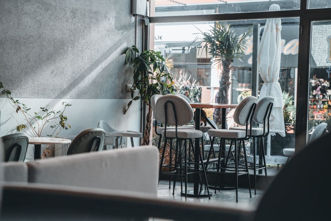 Empty tables and chairs in a quiet cafe with light coming through the front windows