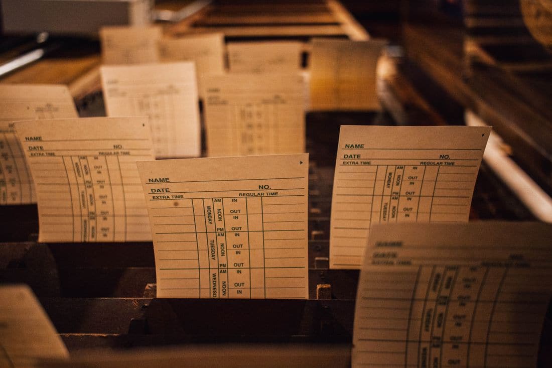 Paper time cards in a wooden rack, with columns for in and out times in the morning, at noon and in the afternoon