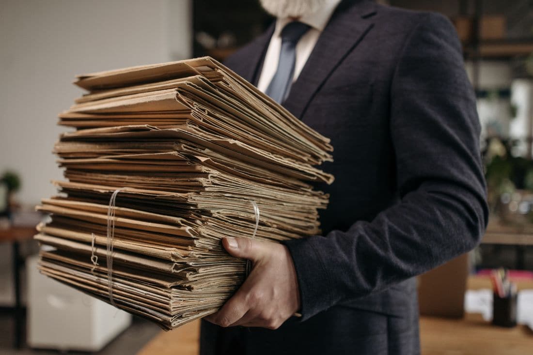 A man in a suit carrying a tied stack of old folders