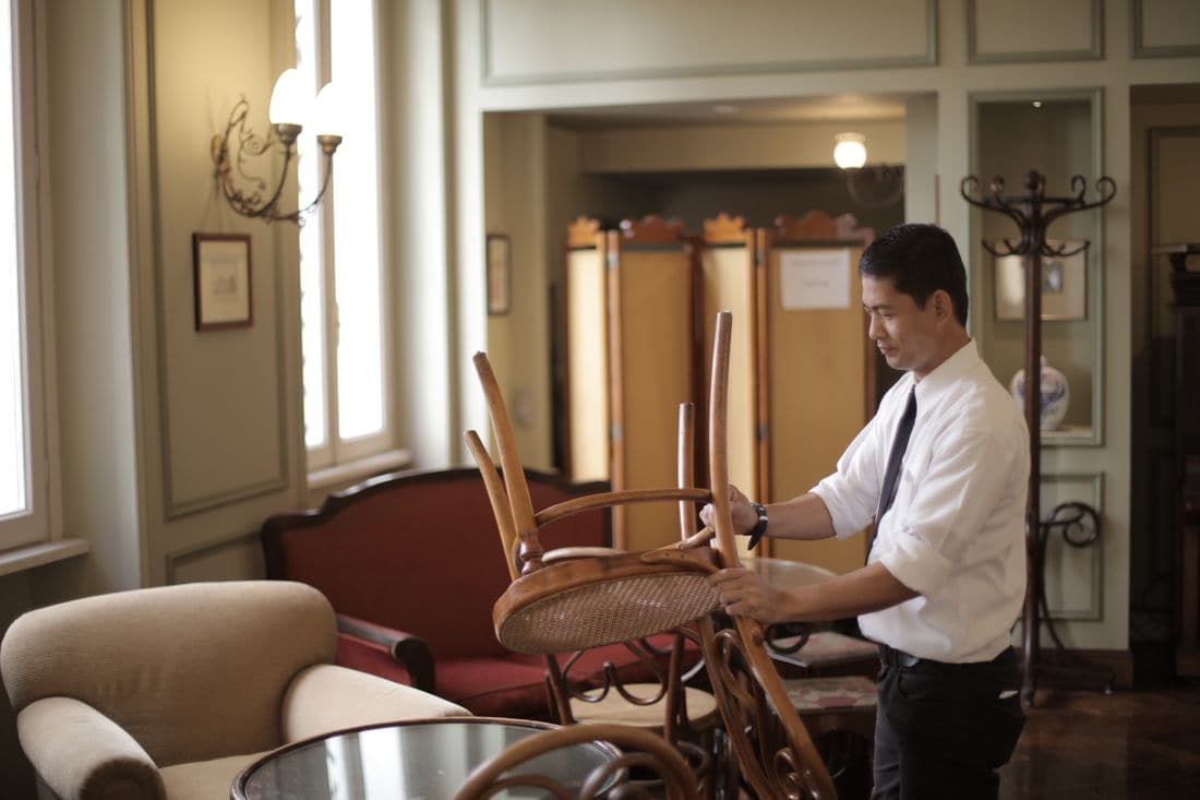 A waiter in a white shirt and tie lifting a chair in an empty dining room
