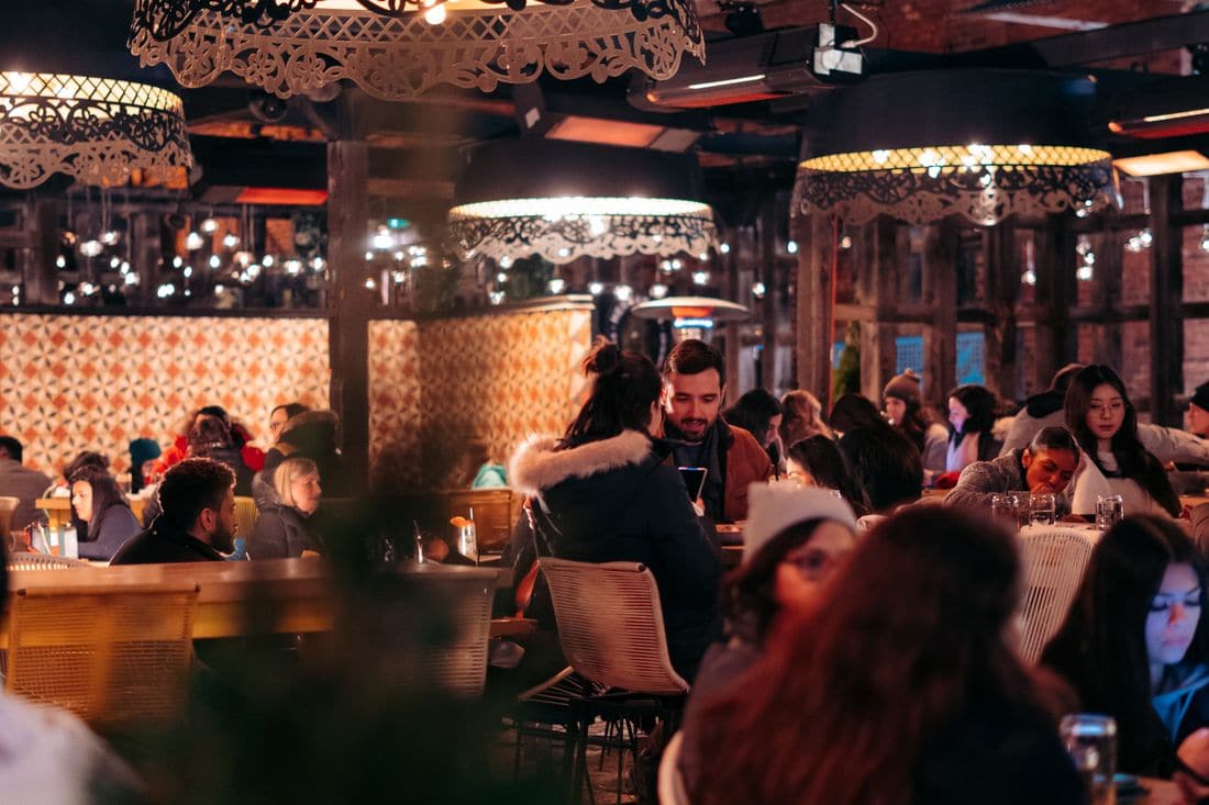 Diners filling the tables of a warmly lit restaurant under large patterned pendant lamps