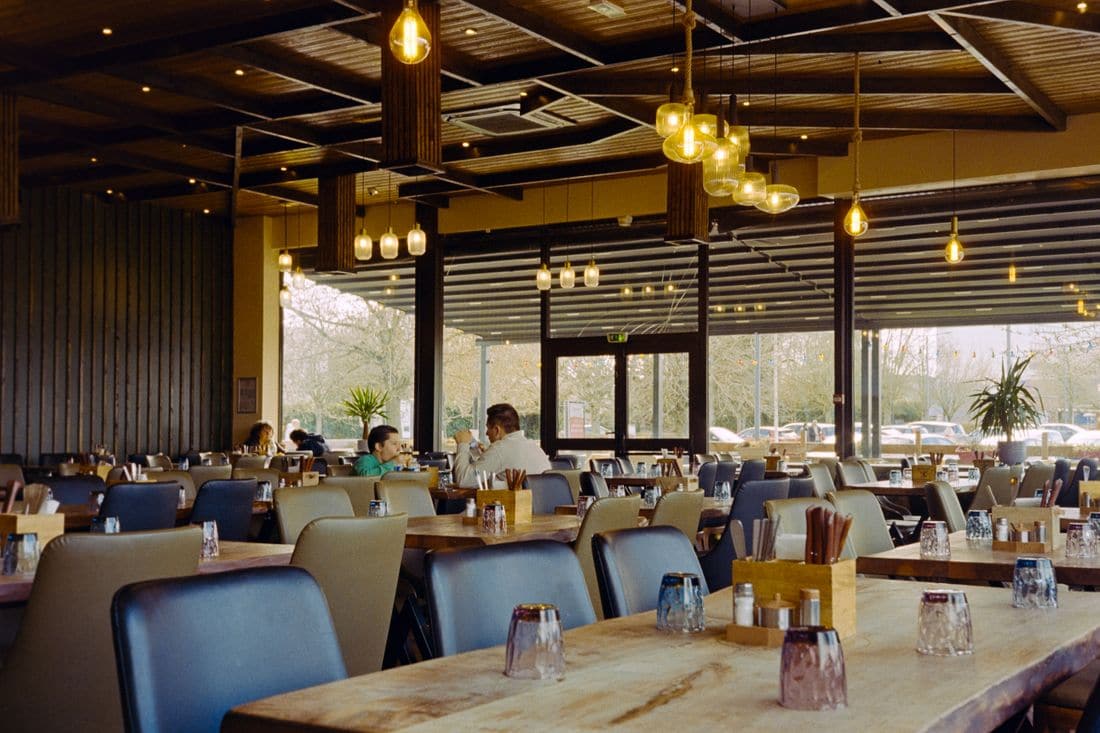 A restaurant in daylight with a handful of diners seated among rows of empty tables and chairs