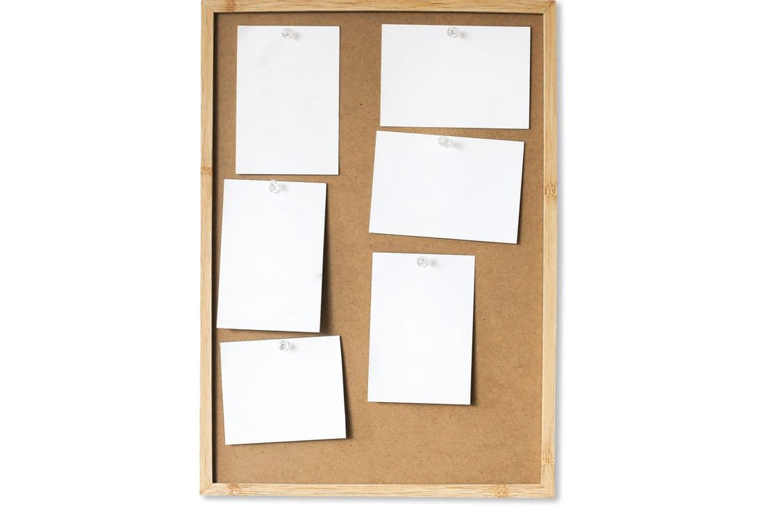 A light wooden framed corkboard with six blank white sheets held on by clear pins