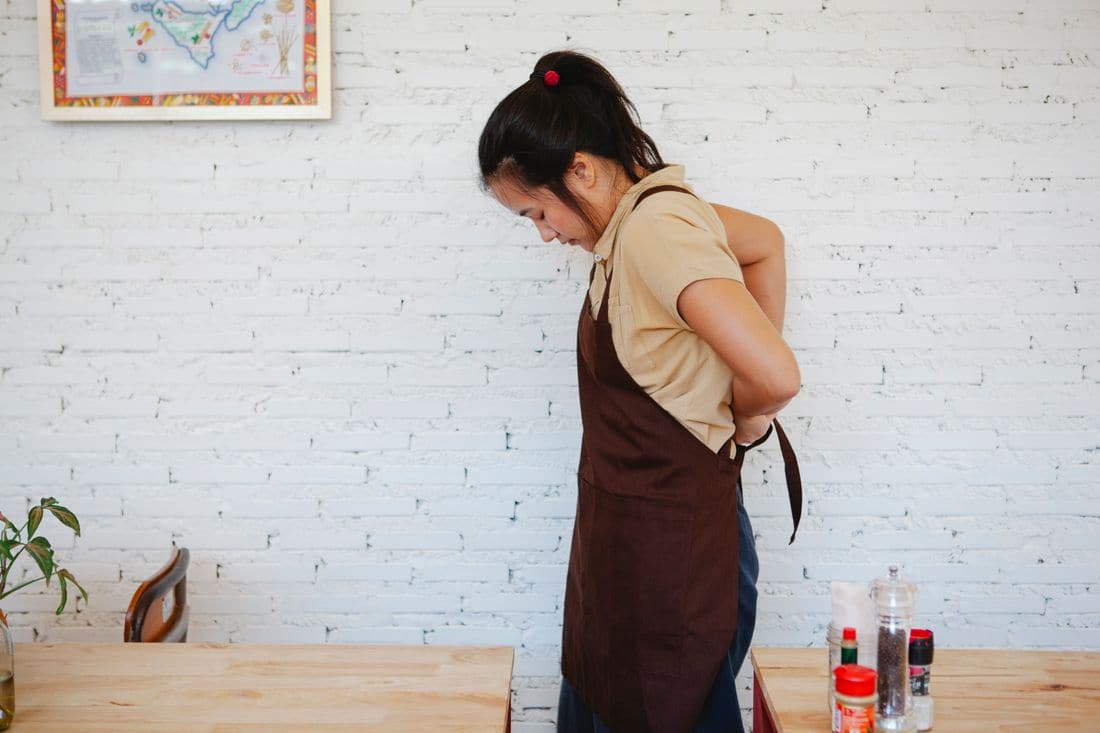 A young worker tying a brown apron in a cafe with white brick walls