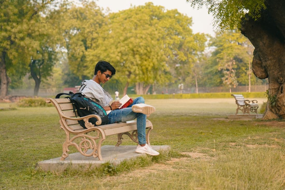 A young man in sunglasses reading a book on a park bench