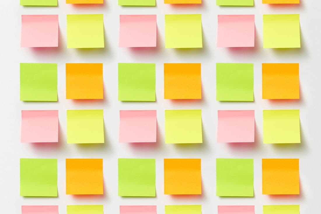 Rows of blank pink, yellow, green and orange sticky notes arranged in a grid on a white surface
