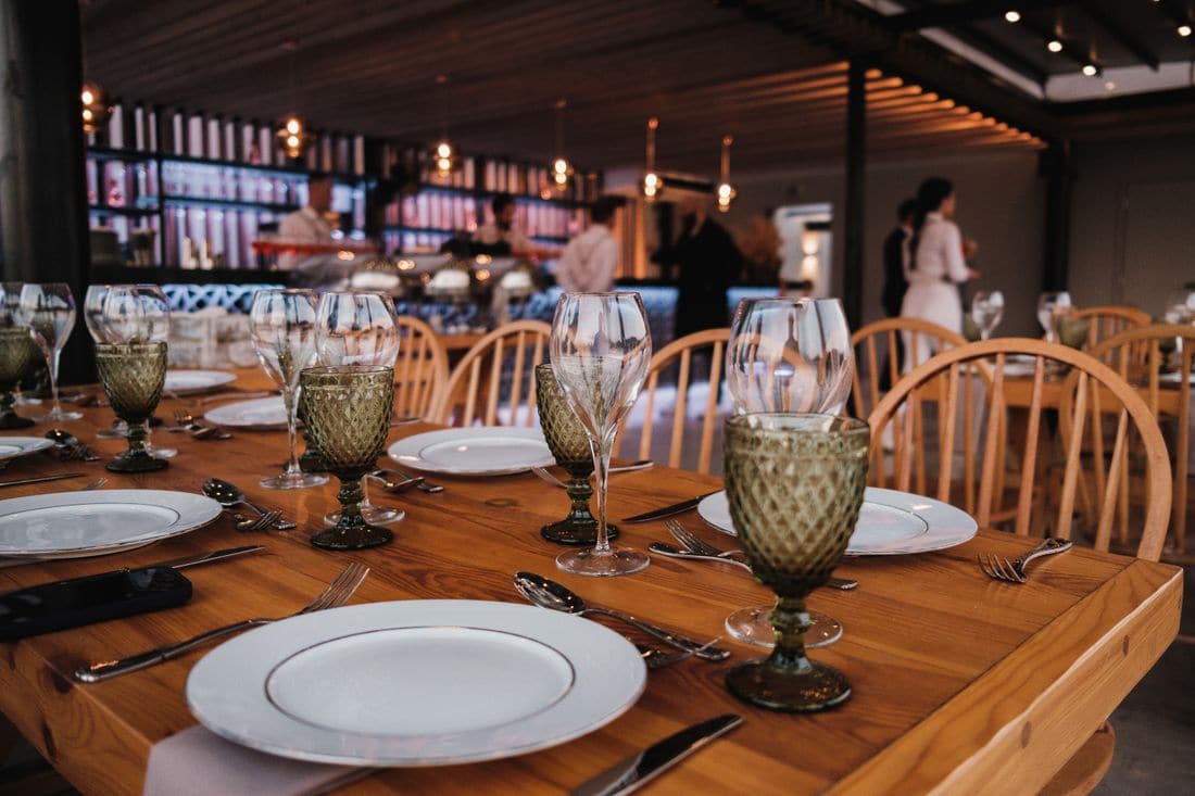 Restaurant tables set with plates and glasses for dinner, with staff in the background