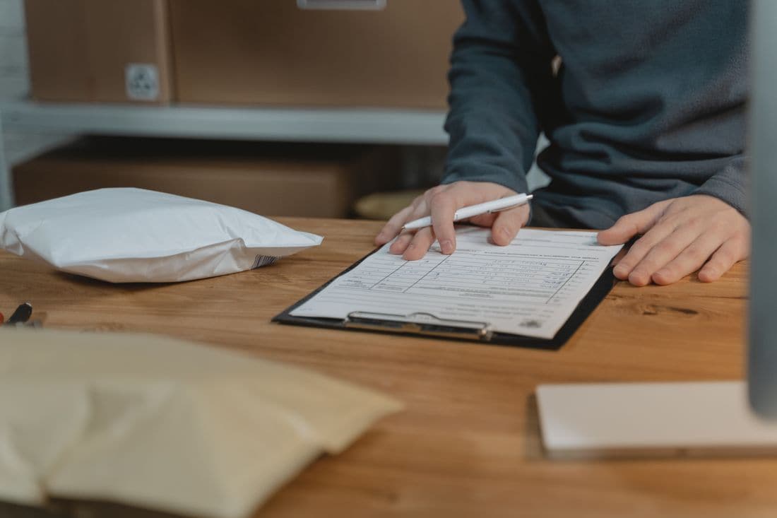 A person with a pen checking a form on a clipboard beside parcels on a desk