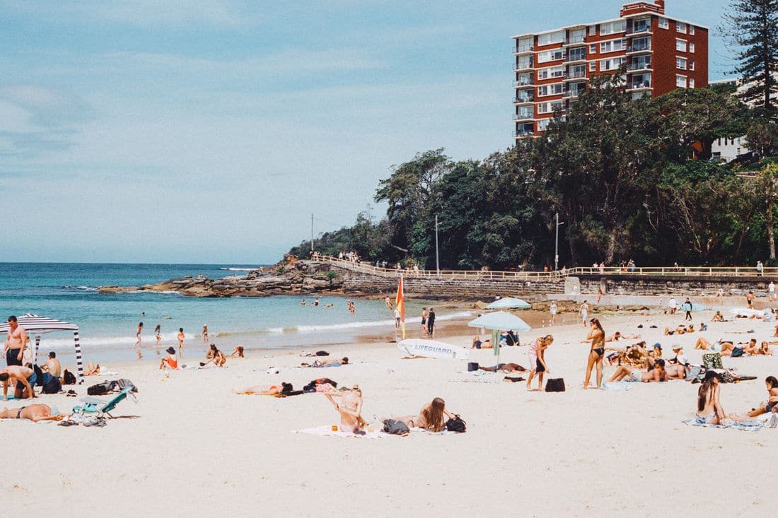 A busy beach on a sunny day with people on the sand and swimmers in the surf
