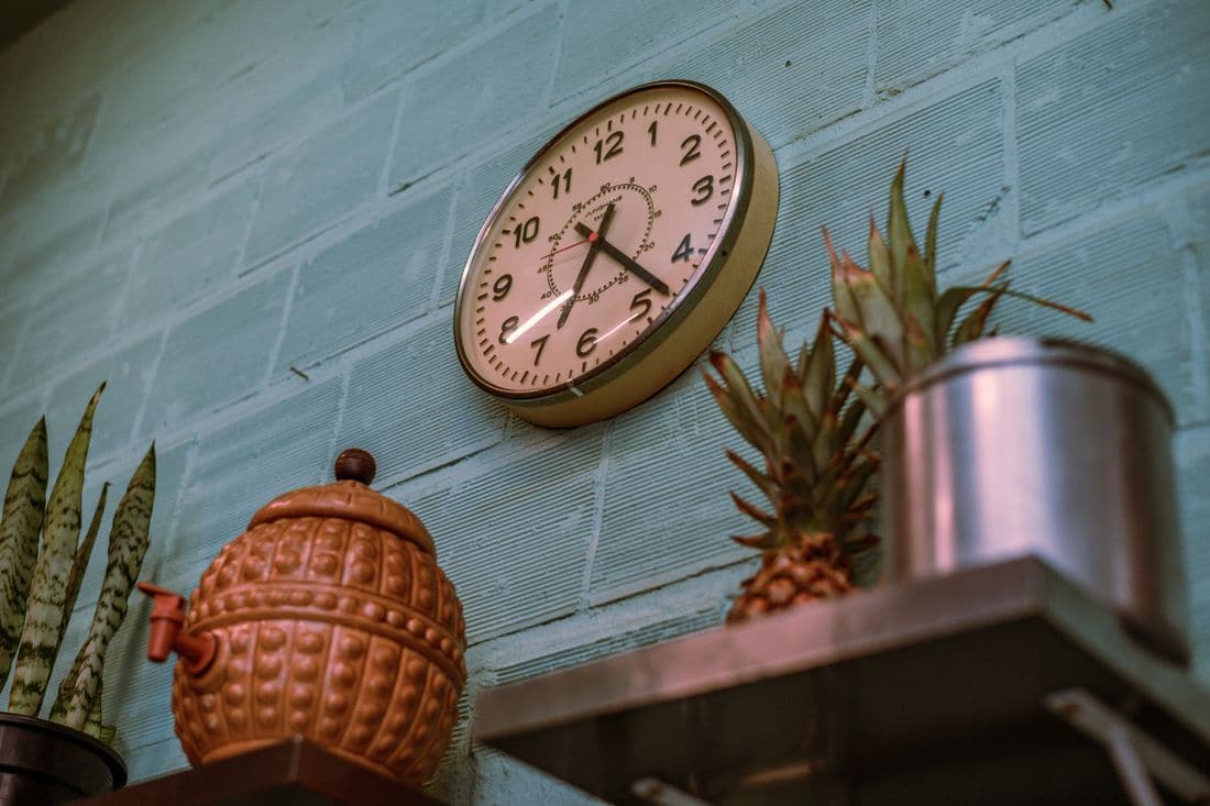 A round wall clock on a painted brick wall above a kitchen shelf