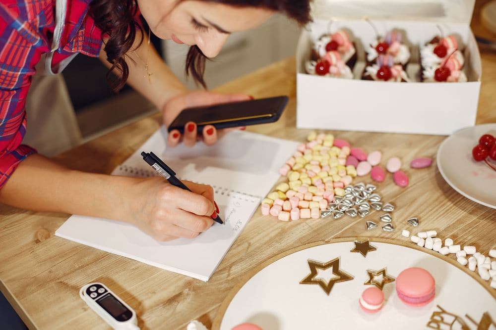 Writing in a notebook with a phone in the other hand