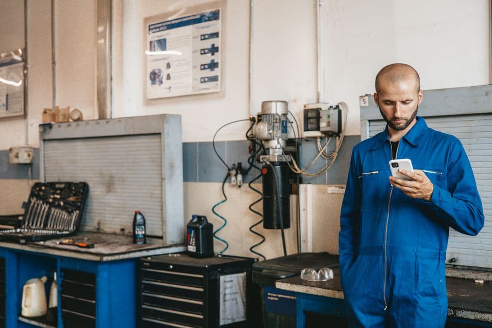 A mechanic in overalls checking a phone in the workshop