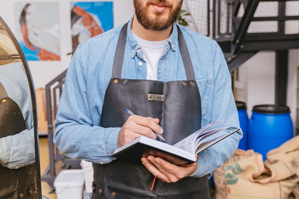 A worker in an apron writing figures in a notebook