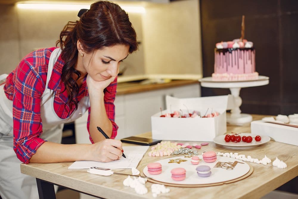 A pastry cook writing in a planner at the kitchen table