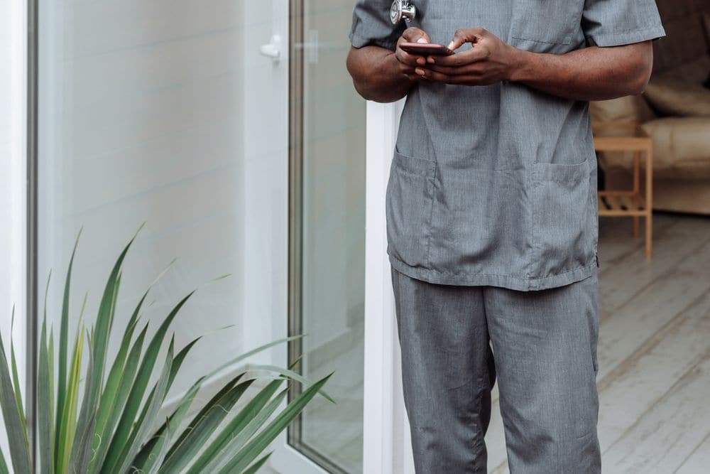 A care worker in scrubs checking a phone