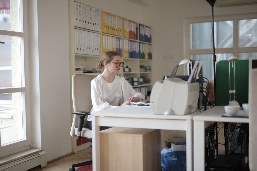 An office worker at a desk in front of shelves of folders