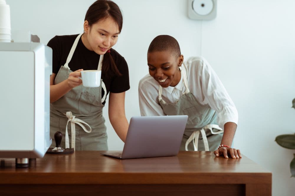 Two baristas looking at a laptop together at the counter