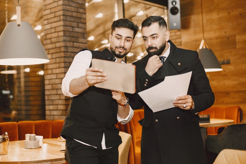 Two men in a restaurant going over papers and a tablet