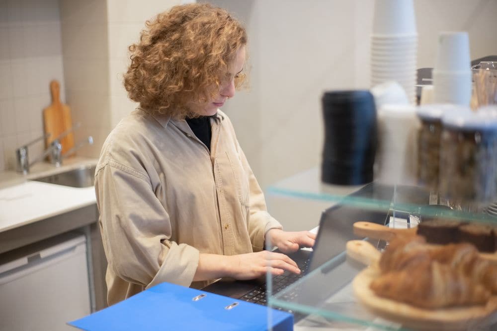 A cafe worker typing on a laptop behind the counter