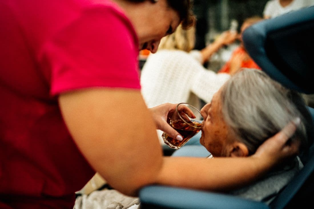 A care worker helping an older woman with a cup of tea