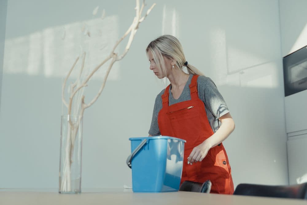 A cleaner with a bucket wiping down a table