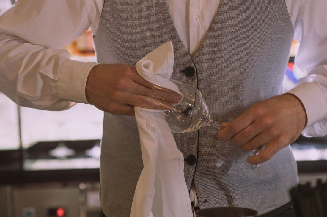 A bartender in a vest polishing a wine glass