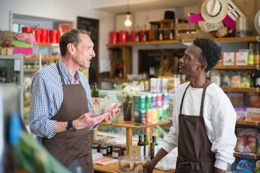 Two grocery store workers in aprons talking in an aisle