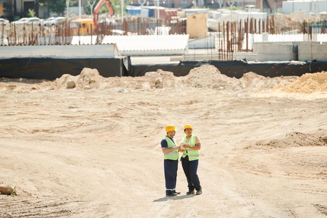 Two workers in safety gear going over plans on a building site