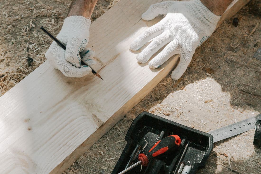 A carpenter in work gloves marking a length of timber