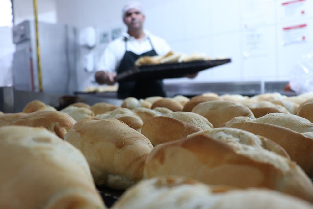 A baker carrying a tray of fresh bread rolls