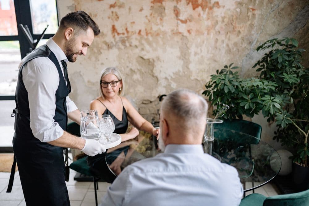 A waiter bringing water to an older couple at their table