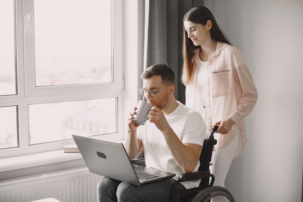 A support worker with a man in a wheelchair working on a laptop